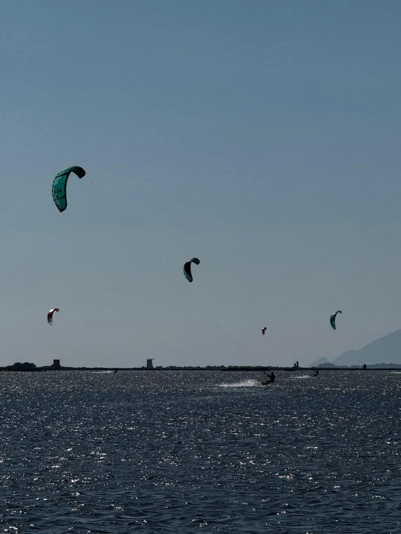 Cinque kite colorati nel cielo azzurro sopra la laguna dello Stagnone, coi mulini sulla riva