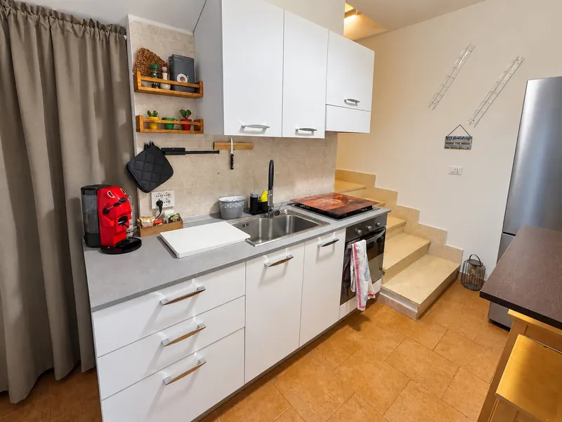La cucina bianca col piano cottura e la macchina del caffè rossa