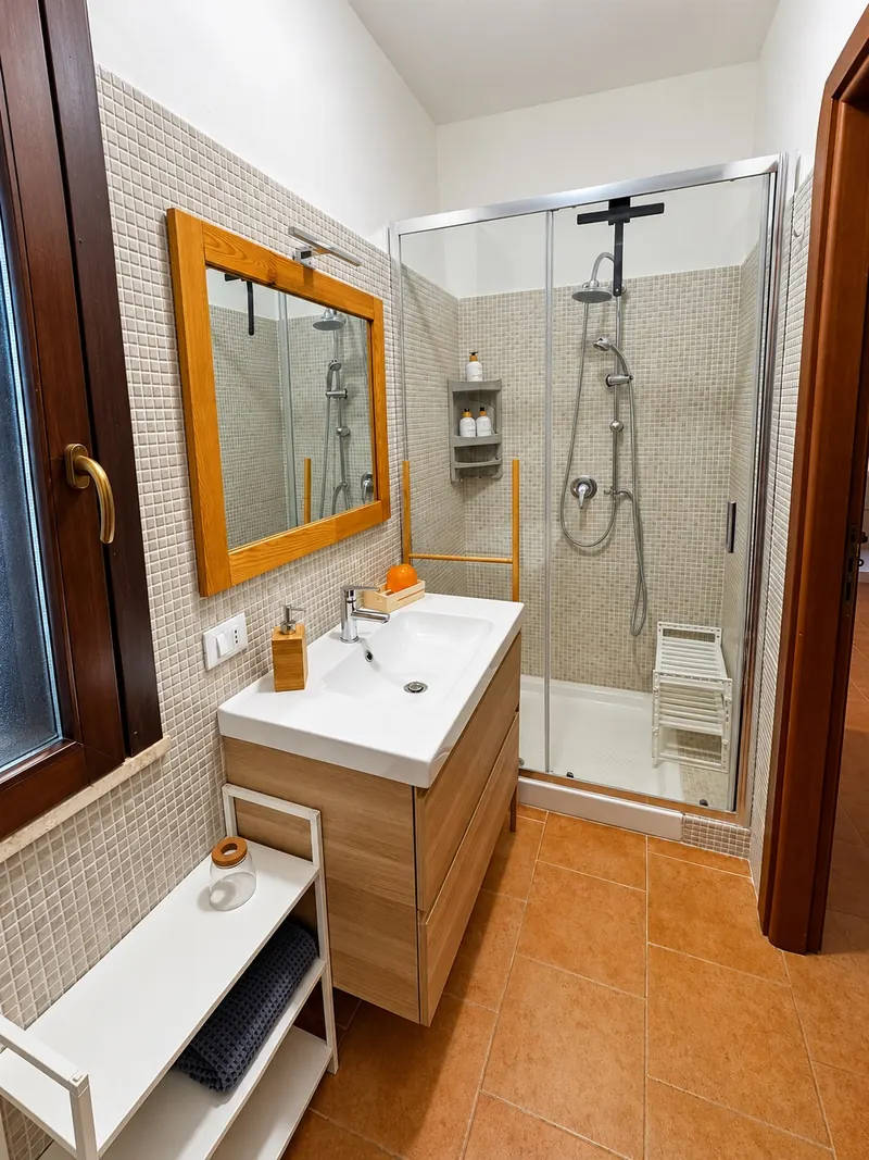 Il bagno col mobile del lavabo in legno, lo specchio e il box doccia