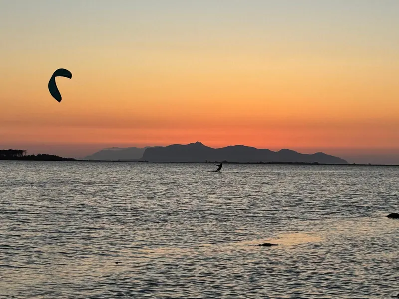 Un kitesurfista in planata al tramonto sulla laguna dello Stagnone, col kite verde nel cielo arancione